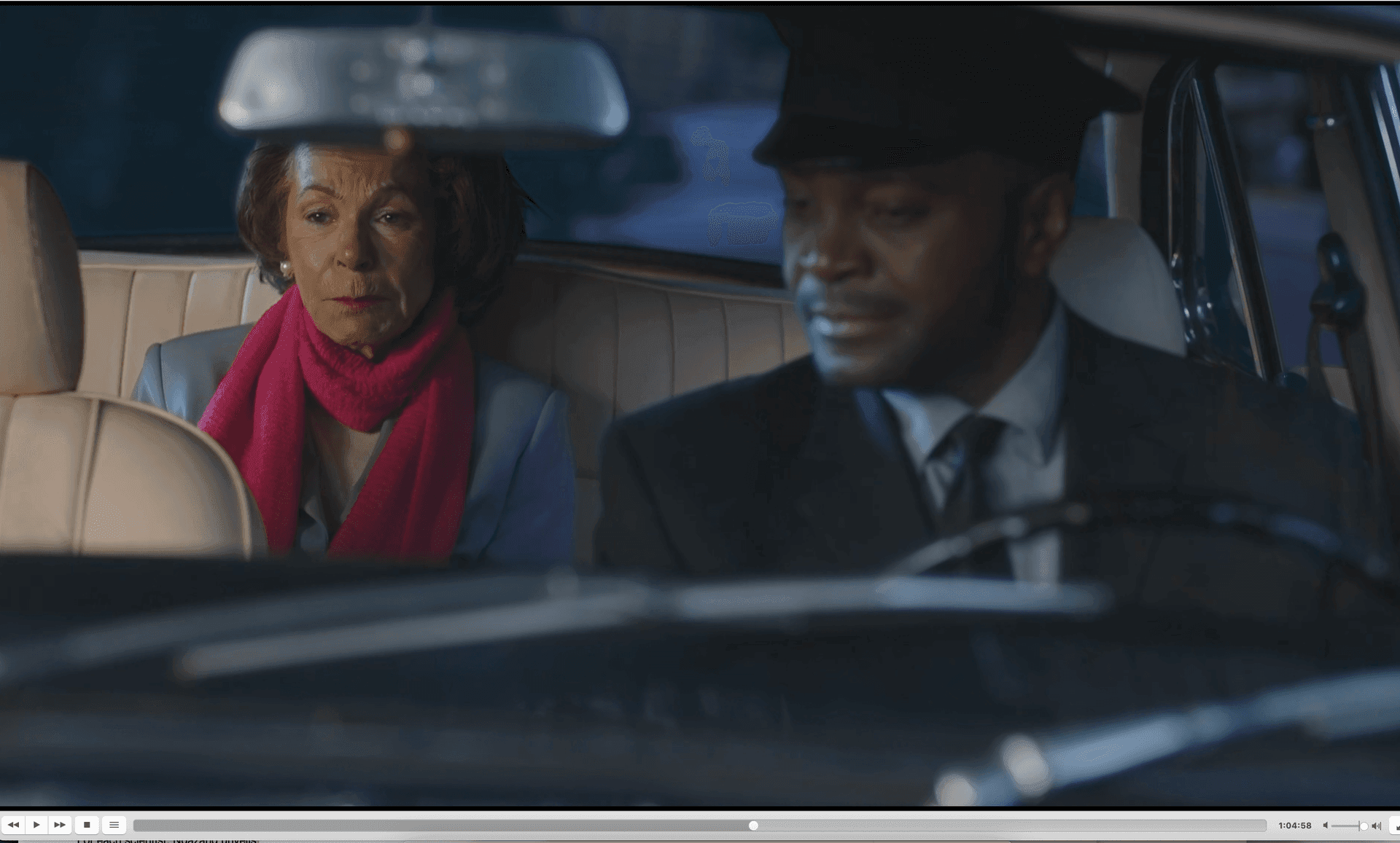 Woman in pink scarf sitting in the backseat of a car with a driver in uniform.